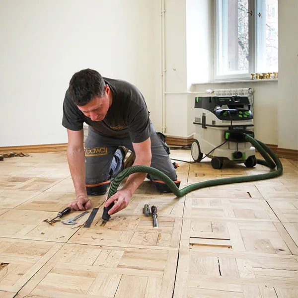 Festool dulkių siurblys naudojamas šalinant senas parketo dalis – meistras Jarekas Gawina darbuojasi Varšuvoje