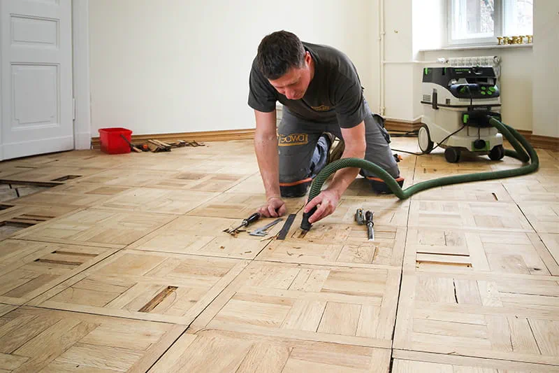 Parketo klojimo meistras Jarekas Gawina atlaisvina sugedusias dalis nuo parketo ir pašalina jas "Festool" Mobilus dulkių siurblys