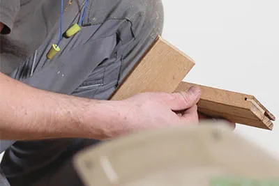 Parketo klojimo meistras Jarekas rankomis tikrina jungiamojo liežuvėlio įstatymo tikslumą lentoje